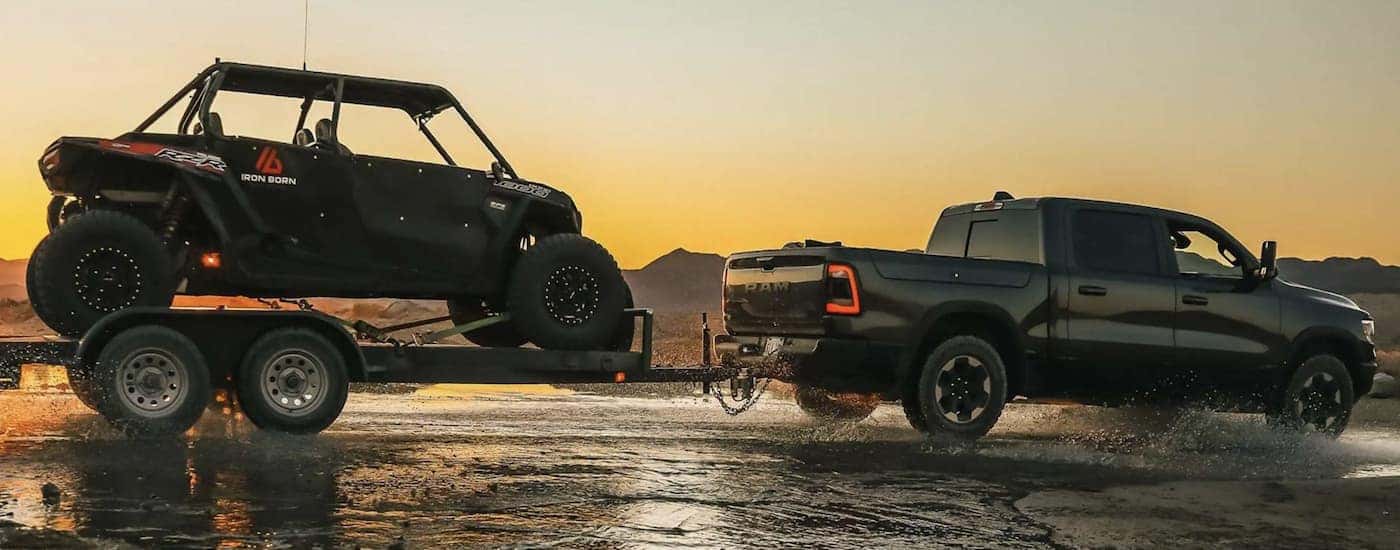 A black 2022 Ram 1500 is shown towing a trailer loaded with an ATV.