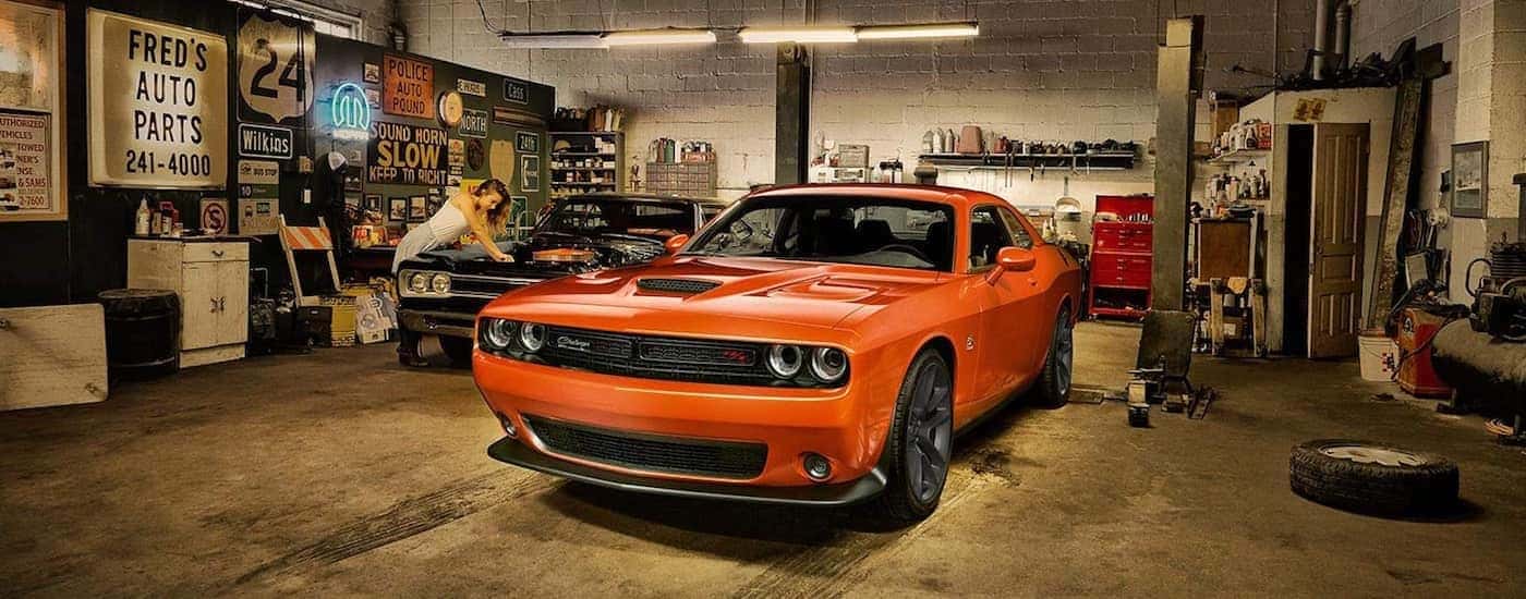An orange 2019 Dodge Challenger is shown parked in a garage near a two post lift.