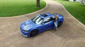 A woman is shown from a high angle leaning against a blue 2020 Dodge Charger.