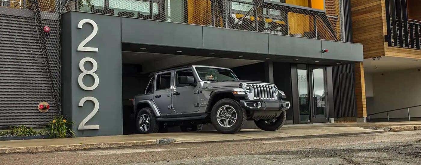 A grey 2020 Jeep Wrangler Sahara Unlimited is shown leaving a parking garage.