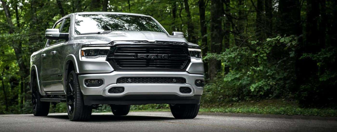 A silver 2020 Ram 1500 is shown from a low angle driving on a wooded road.