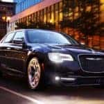 A popular Certified Pre-Owned Chrysler, a black 2019 Chrysler 300, is shown driving on a city street at night.
