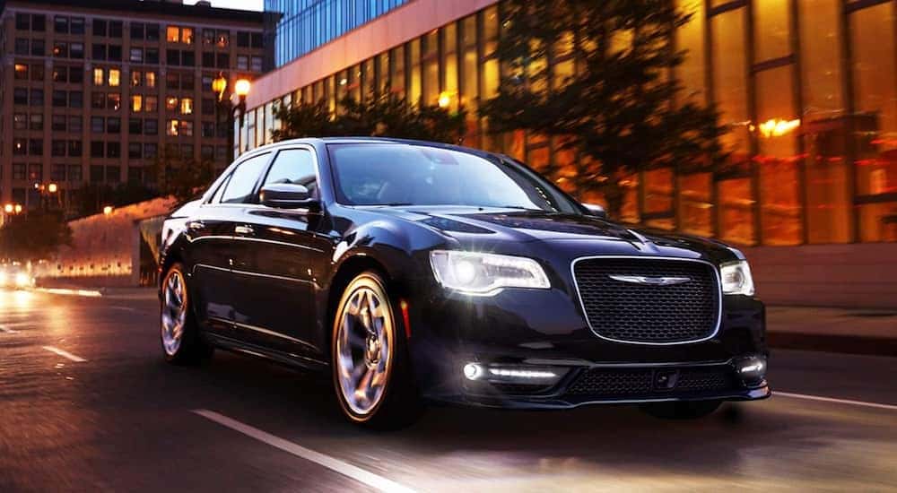 A popular Certified Pre-Owned Chrysler, a black 2019 Chrysler 300, is shown driving on a city street at night.