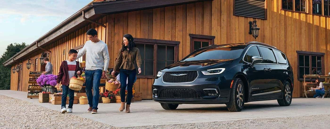 A black 2020 Chrysler Pacifica is shown next to a barn and family at an apple orchard.