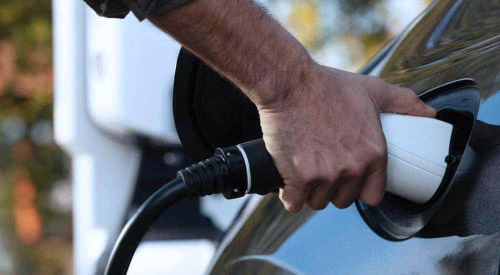 A person is shown plugging a charge cable into a grey 2020 Chrysler Pacifica Hybrid.
