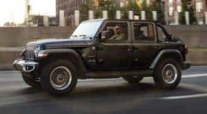 A black 2022 Jeep Wrangler is shown from the side driving through a city.