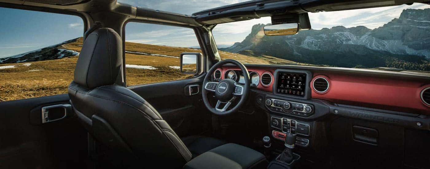 The black interior of a 2022 Jeep Wrangler shows the steering wheel and infotainment screen.