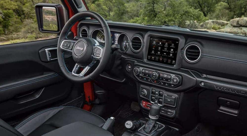 The black interior of a 2022 Jeep Wrangler shows the steering wheel and infotainment screen.