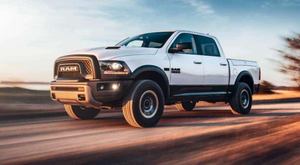 A white 2018 Ram 1500 is shown from the side driving on an open road.