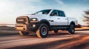 A white 2018 Ram 1500 is shown from the side driving on an open road.