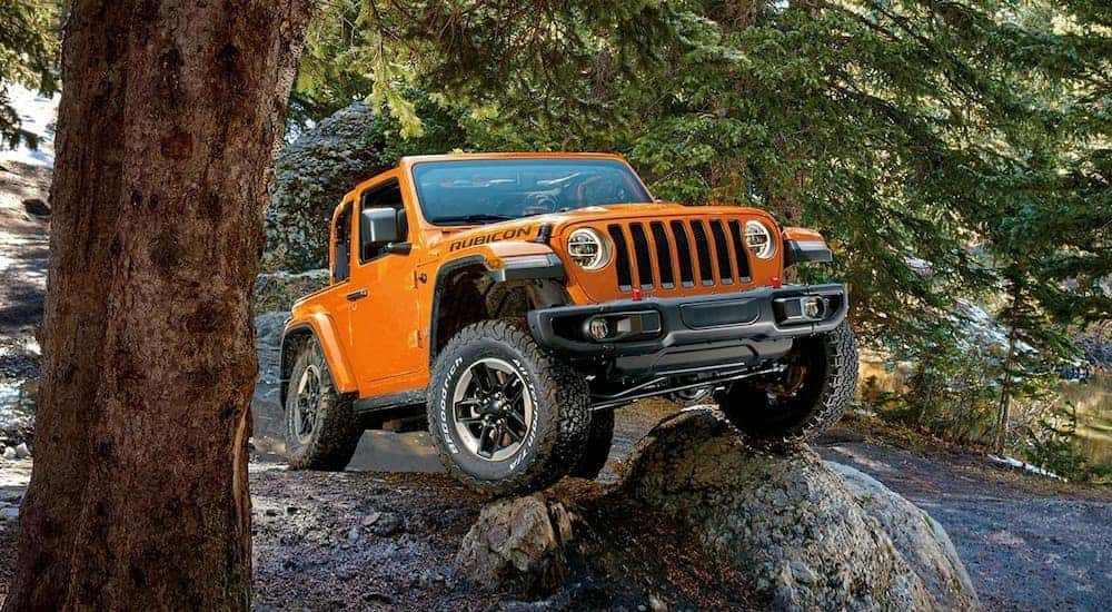 An orange 2019 Jeep Wrangler Rubicon is shown from the front as it climbs over a rock.