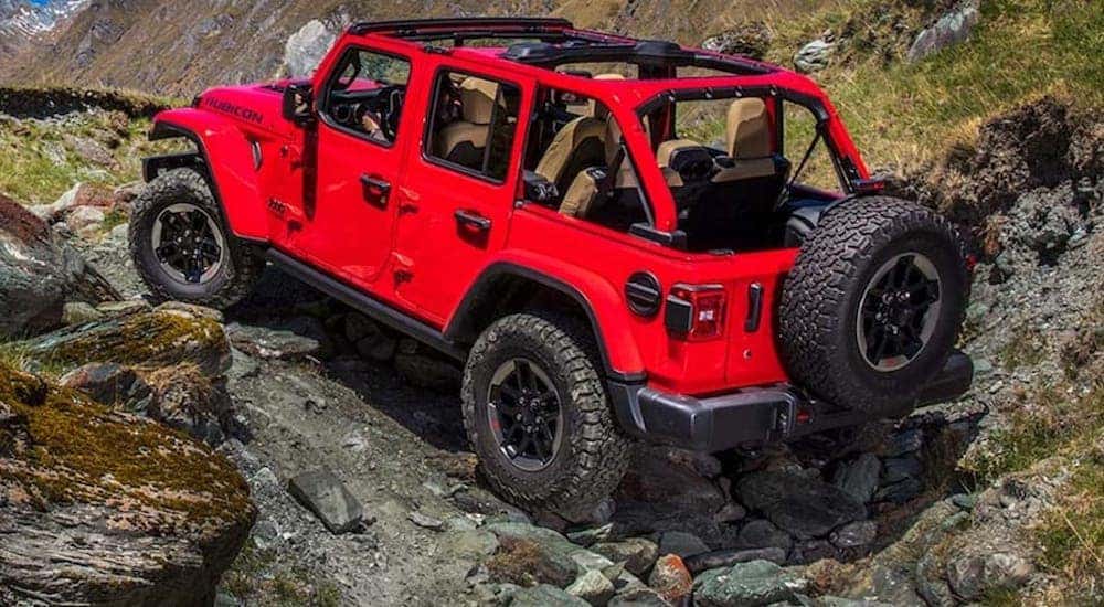A red 2022 Jeep Wrangler is shown from the rear as it traverses a rocky area.