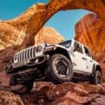 A white 2022 Jeep Wrangler Rubicon is shown from the front at a low angle while parked on red rocks after the owner read a Wrangler buyer's guide.