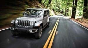 A silver 2019 Jeep Wrangler is shown from the front driving on an open tree lined road after leaving a used Jeep Wrangler dealer.
