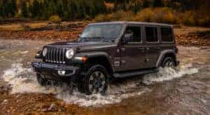 A black 2018 Jeep Wrangler is shown from the side driving through a river.