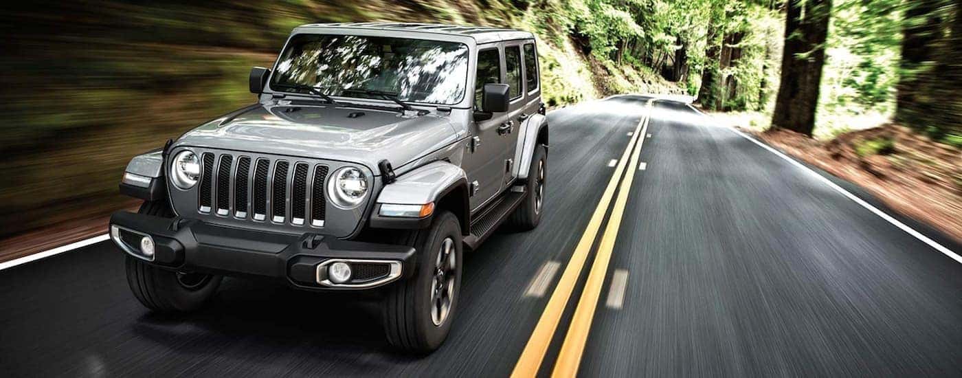 A grey 2019 Jeep Wrangler is shown driving on an open road after looking at a Wrangler buyer's guide…