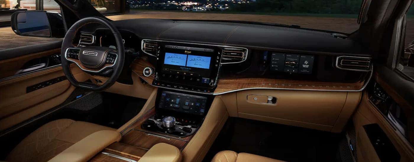 The tan and black interior of a 2023 Wagoneer L shows the steering wheel and infotainment screen.