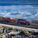 A red 2023 Wagoneer L is shown from the side while towing a boat after leaving a Wagoneer L dealership.