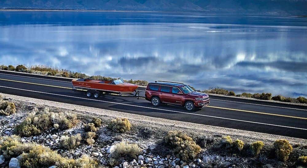 A red 2023 Wagoneer L is shown from the side while towing a boat after leaving a Wagoneer L dealership.