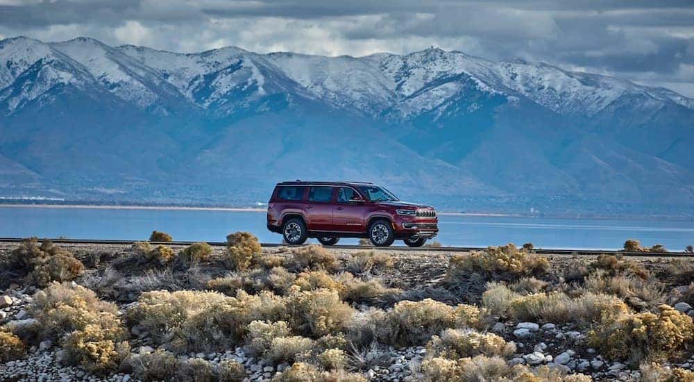 A red 2023 Wagoneer L is shown from the side on a lakeside road.