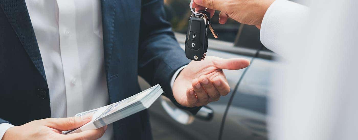 A salesperson is shown trading cash of a set of car keys.