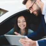 A car salesman is shown speaking to a customer about how to value their trade.