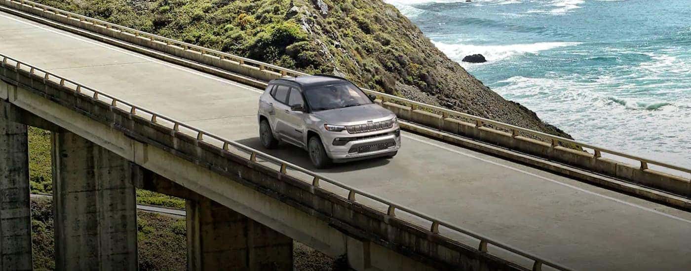 A grey 2022 Jeep Compass is shown driving on a bridge.