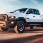 A white 2018 Ram 1500 is shown driving on an open road.