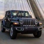 A black 2023 Jeep Wrangler Unlimited is shown driving over a bridge.