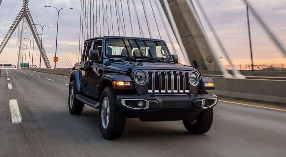 A black 2023 Jeep Wrangler Unlimited is shown driving over a bridge.
