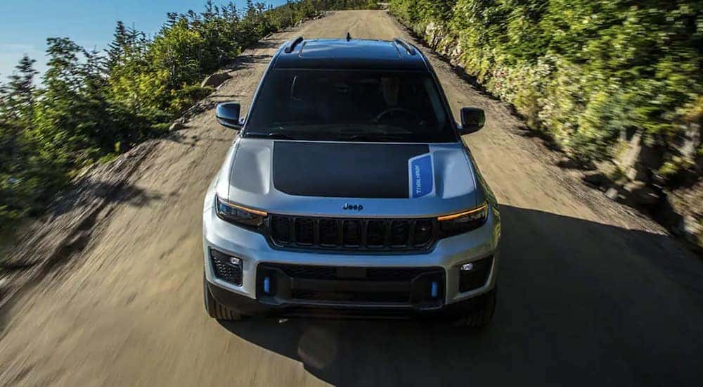 A popular used Jeep SUV for sale, a grey 2023 Jeep Grand Cherokee 4xe, is shown from the front driving on an open dirt road.