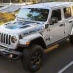 A white 2023 Jeep Wrangler 4xe is shown from the side driving on an open.