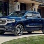 A blue 2023 Ram 1500 is shown from the side parked in front of a house.