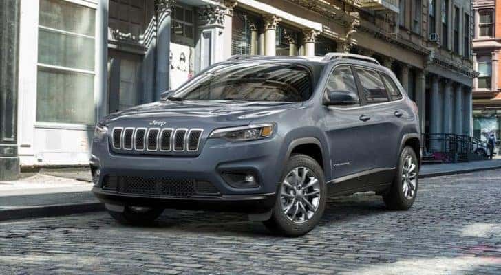A grey 2021 Jeep Cherokee is shown from the side parked on a stone street.