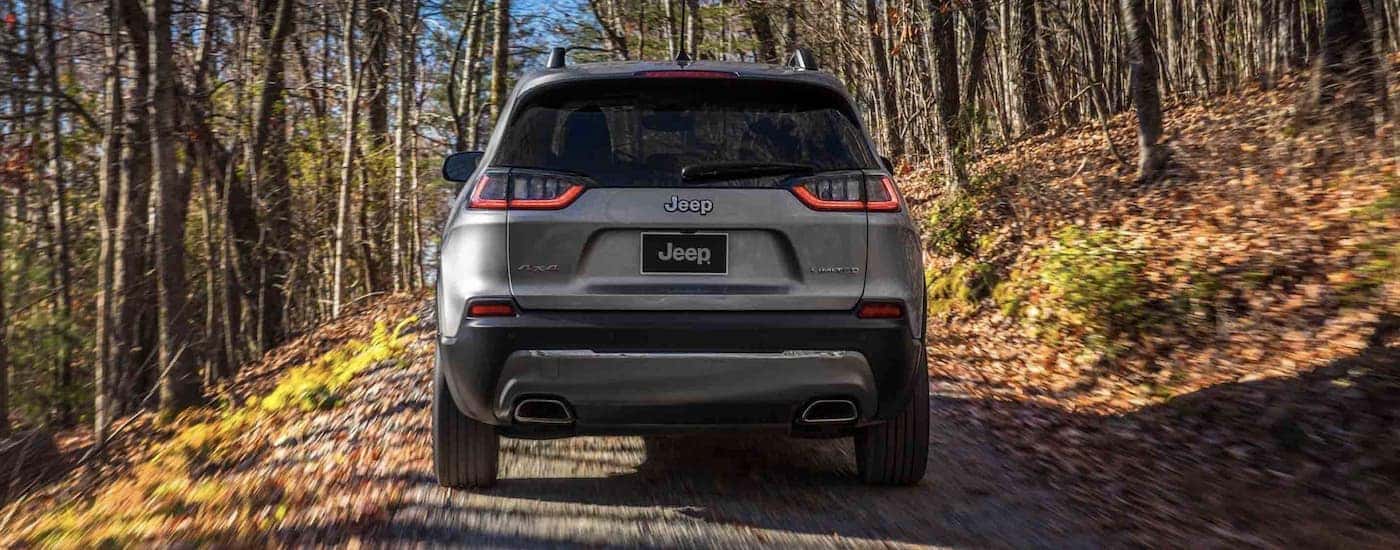 A grey 2022 Jeep Cherokee Limited is shown from the rear driving on a dirt road.