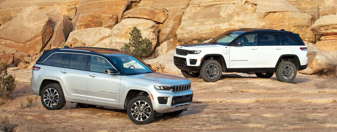 A silver and a white 2023 Jeep Grand Cherokee are shown parked in a dirt lot.