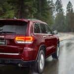 A red 2020 Jeep Grand Cherokee Limited is shown from the rear driving on a road after visiting a used SUV dealer.