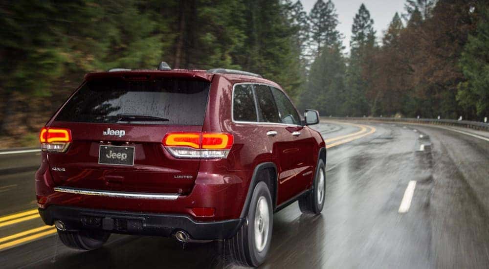 A red 2020 Jeep Grand Cherokee Limited is shown from the rear driving on a road after visiting a used SUV dealer.