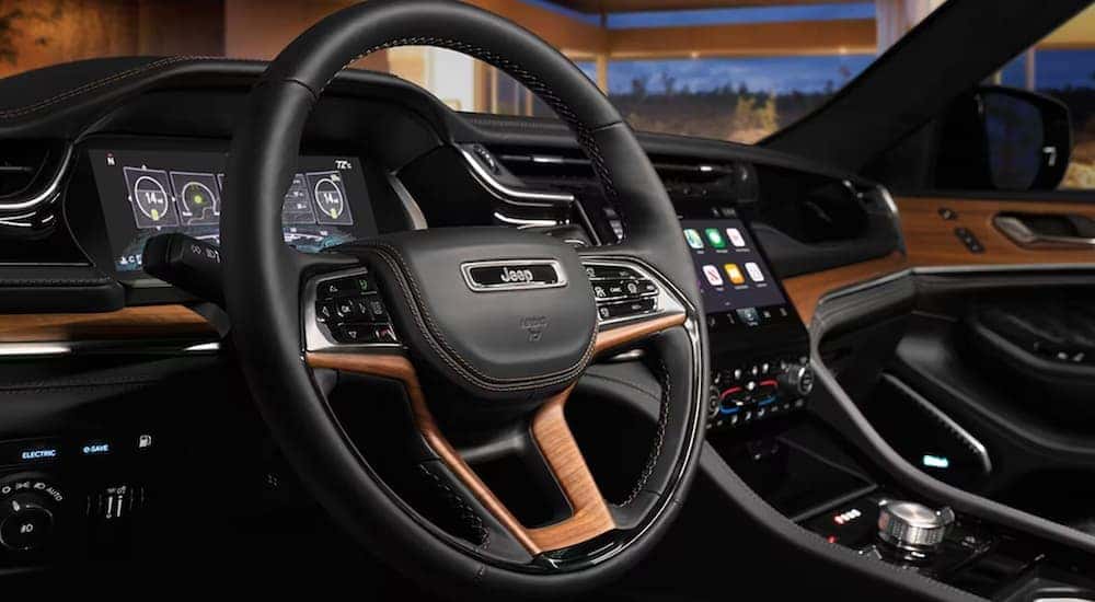 The black interior of a 2023 Grand Cherokee shows the steering wheel and infotainment screen.