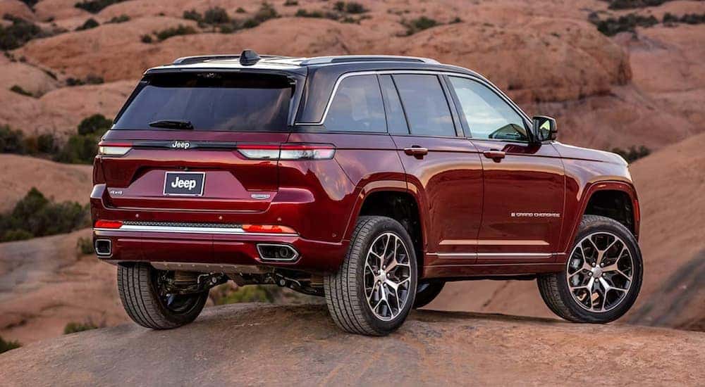 A popular Jeep Grand Cherokee for sale near Covington, KY, a red 2023 Grand Cherokee, is shown from the rear parked on a rock.