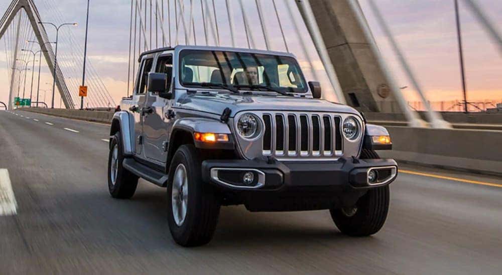 A grey 2021 Jeep Wrangler is shown from the front driving over a bridge.