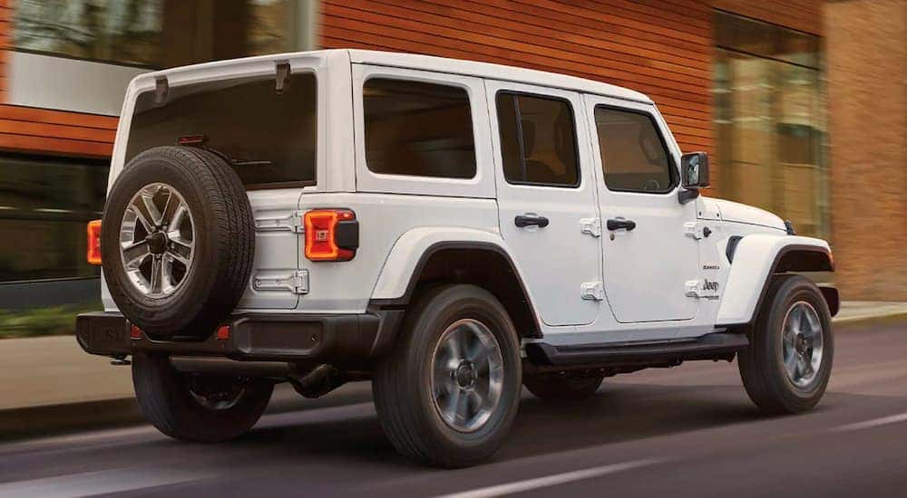 A white 2022 Jeep Wrangler is shown from the rear driving on an open road.