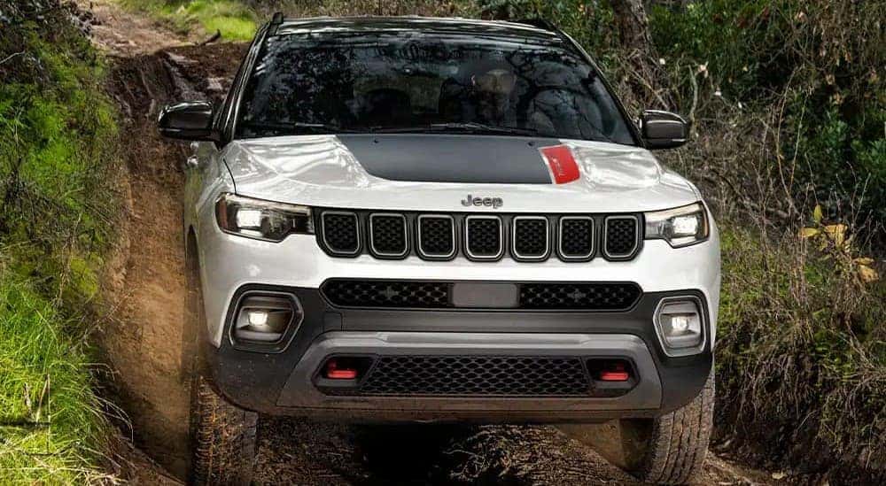 A white and black 2023 Jeep Compass Trailhawk is shown off-roading on mud.