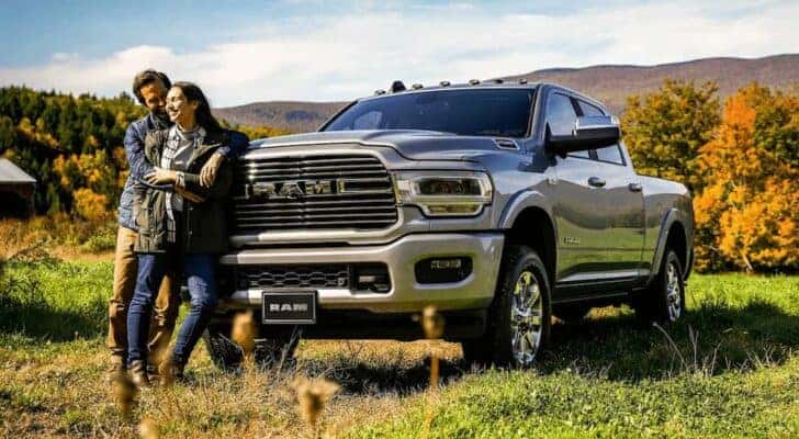 A couple is shown standing in front of a silver 2022 Ram 2500 parked in an open field.