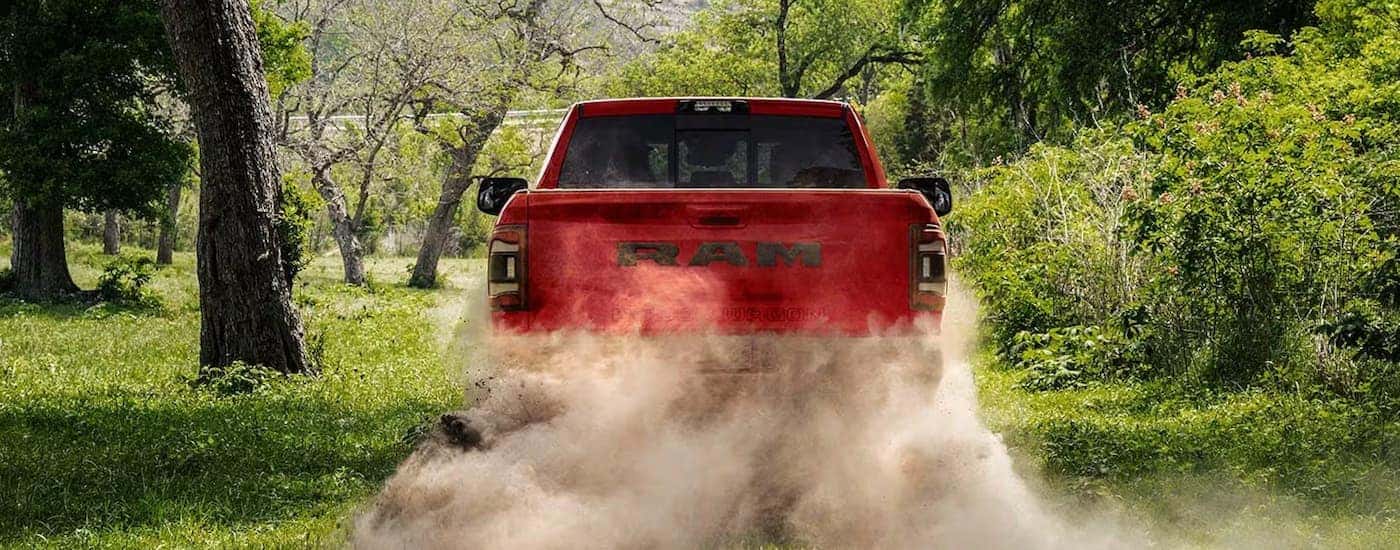 A red 2023 Ram 2500 Power Wagon is shown from the rear driving on a dusty dirt road.