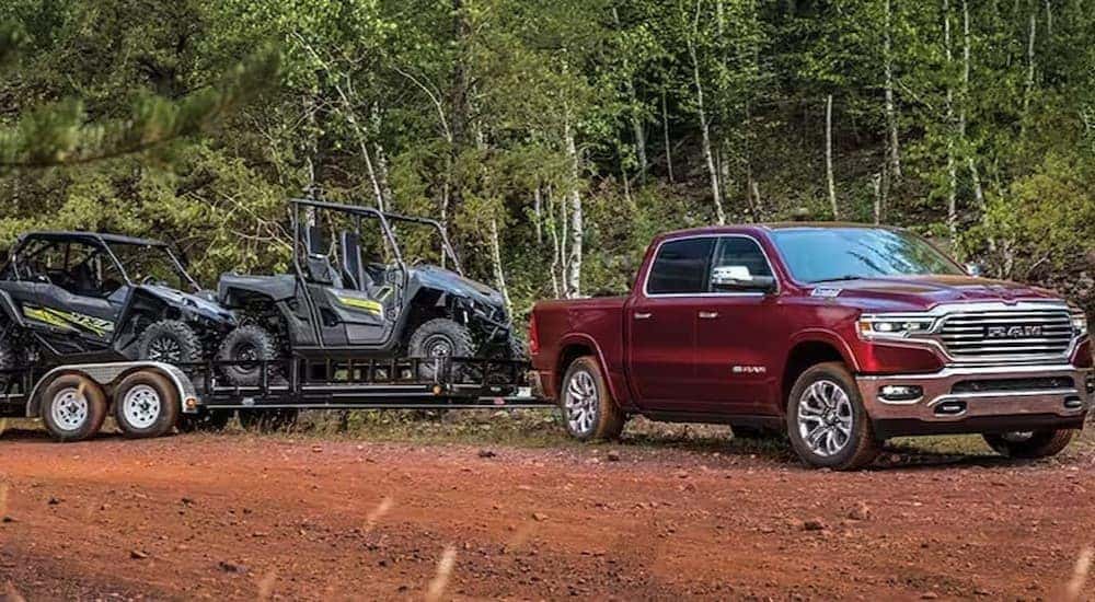 A red 2023 Ram 1500 is shown towing a trailer off-road.