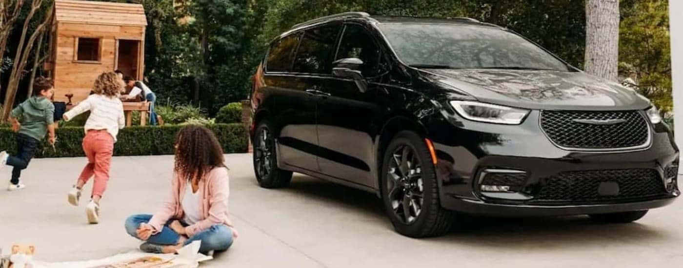 a black 2023 Chrysler Pacifica is shown parked on a driveway near a tree fort.