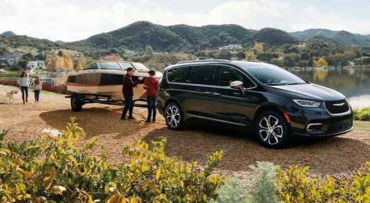 A black 2023 Chrysler Pacifica for sale near Burlington, KY is shown towing a boat near a lake.