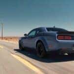 A blue 2023 Dodge Challenger Scat Pack is shown from the rear at an angle driving down a rural highway.