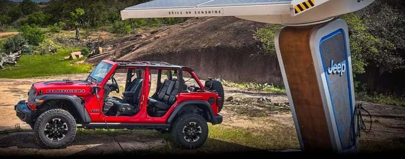 A red 2024 Jeep Wrangler 4xe Rubicon is shown parked near a charge station.
